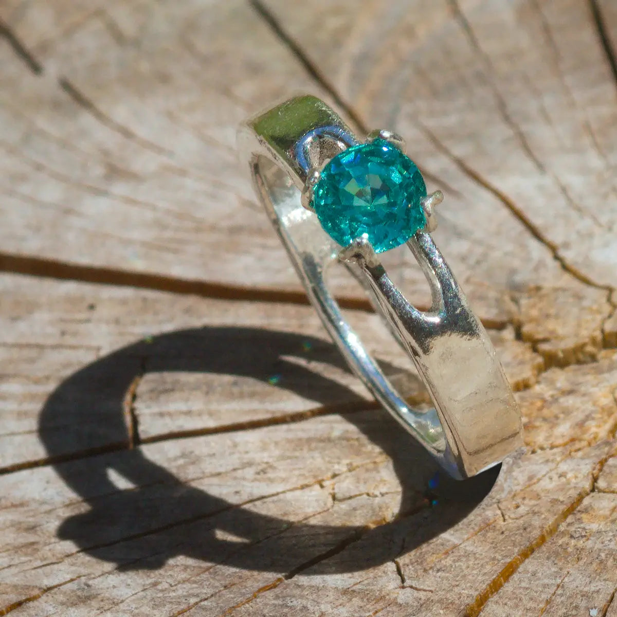 Silver ring with a bright blue green parabia yag garnet gemstone on a wooden surface