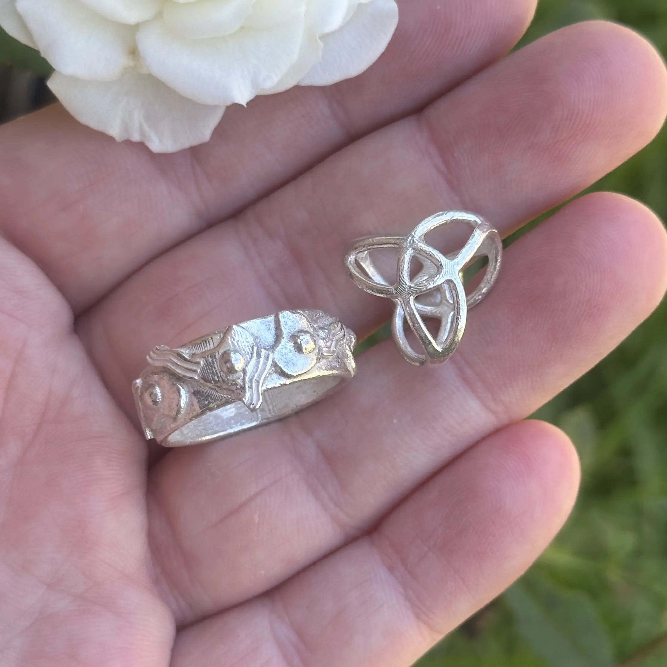 Two cast silver pieces held in a hand with a white rose in the background
